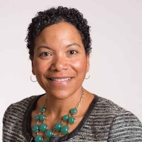 Cathy Estelle is pictured from the shoulders up - with a tweed blazer, green necklace, short hair and hoop earrings